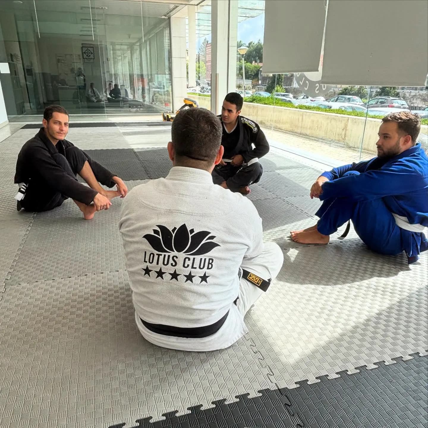 Alunos sentados no tatame a ouvir o professor, de costas com o quimono da Lotus Club