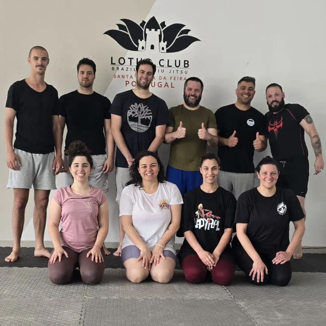 Grupo do treino da manhã junto à parede com o logótipo da academia