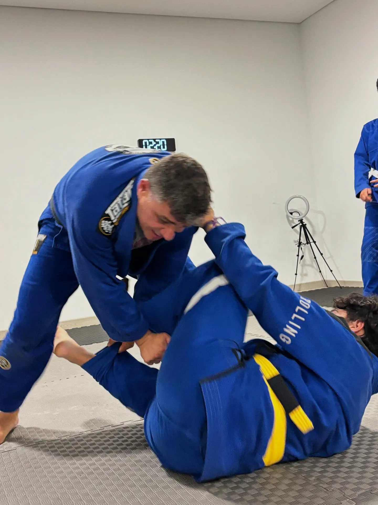 Dois alunos de quimono azul a treinar uma passagem de guarda