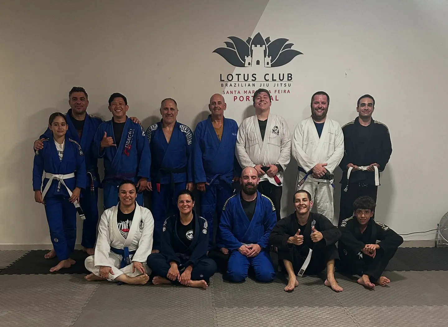 Turma de adultos de quimono azul, branco e preto em frente ao logótipo da Lotus Club